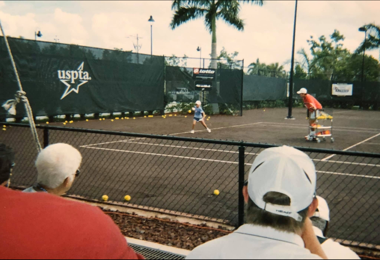 Junior player training on a clay court beside a USPTA banner