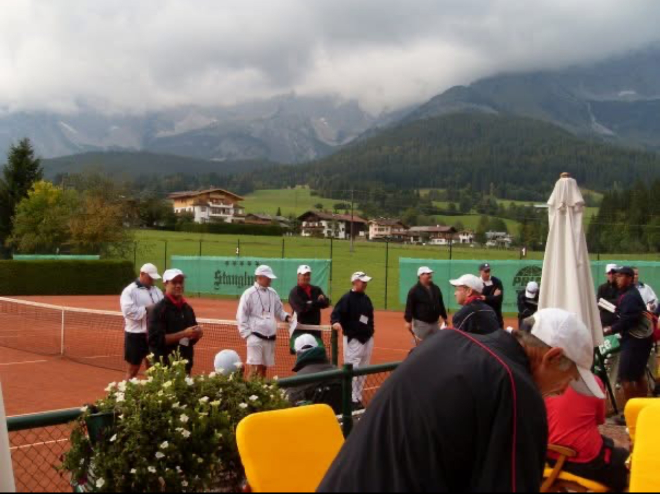 Coaches gathered at a clay court with mountains in the background