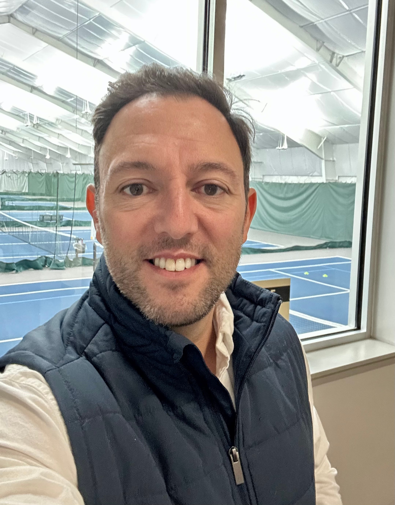 Mike Manzella inside an indoor tennis facility overlooking blue courts