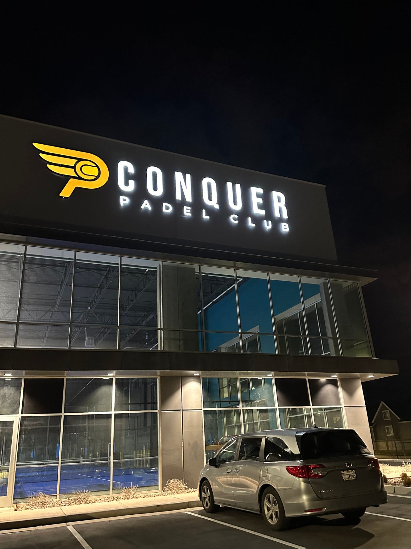 Exterior of Conquer Padel Club lit up at night